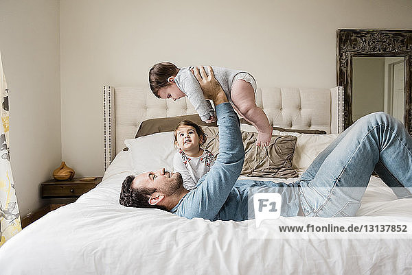Playful father lifting son while lying by daughter on bed at home
