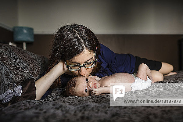 Mutter küsst neugeborenen Sohn  der zu Hause auf dem Bett liegt