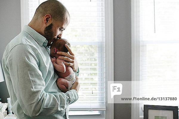 Side view of father kissing newborn daughter while carrying her at home