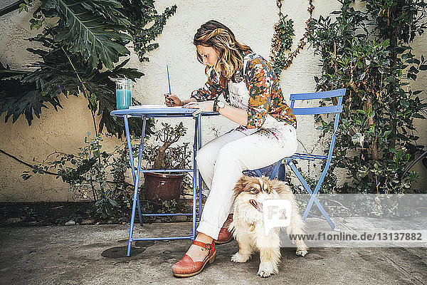 Gemälde des Künstlers in voller Länge  während er mit einem Hund auf einem Stuhl im Hinterhof sitzt