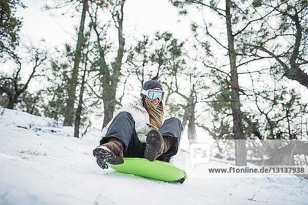 Happy woman riding on sled in snow covered field