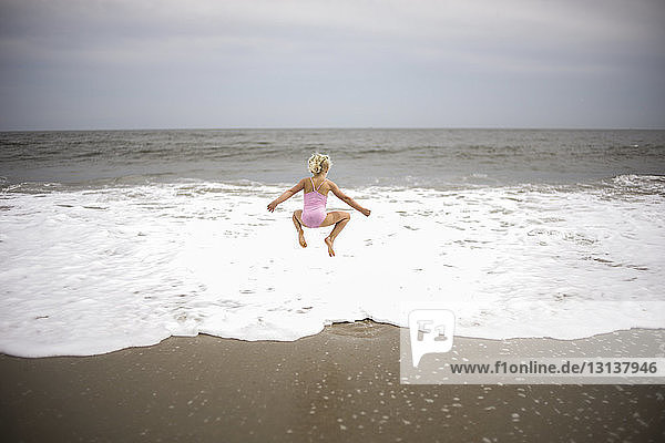 Rear view of playful girl jumping on shore at beach against sky