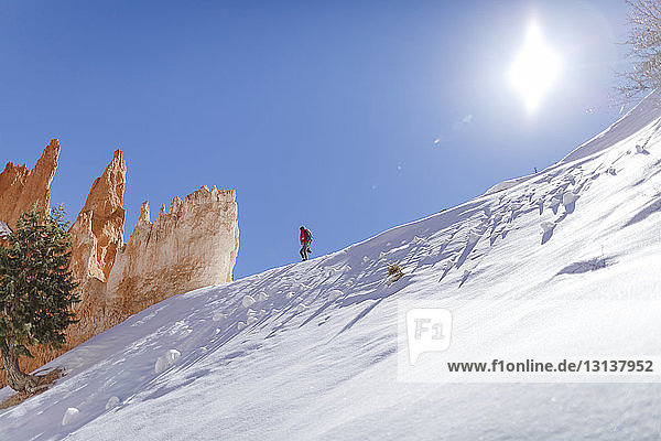 Niedrigwinkelansicht eines Wanderers  der am sonnigen Tag auf einem schneebedeckten Berg gegen den Himmel läuft