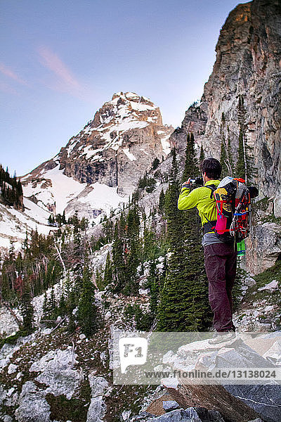 Hiker photographing while standing on rock against mountains