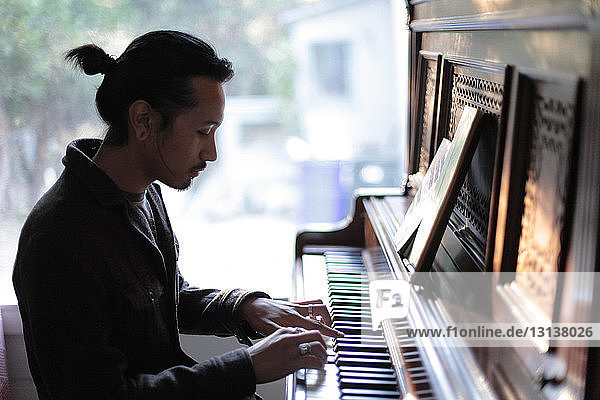 Mann spielt zu Hause Klavier gegen Fenster