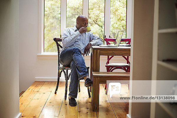 Älterer Mann benutzt Laptop  während er zu Hause Kaffee trinkt