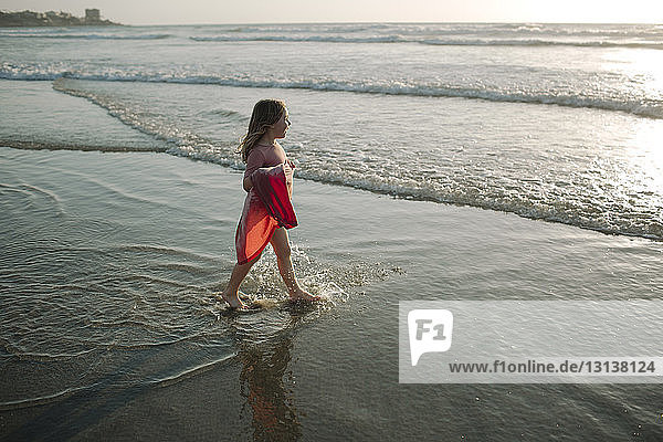 High angle view of girl holding dress while walking towards sea at beach