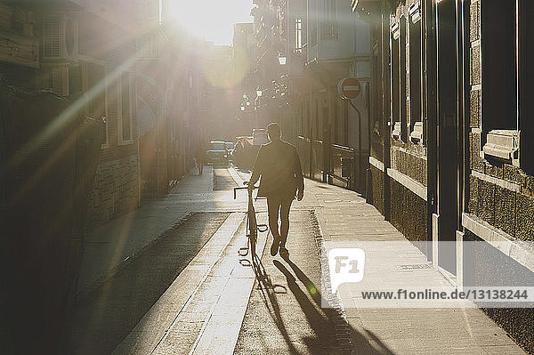 Rückansicht eines Mannes  der bei Sonnenuntergang mit dem Fahrrad auf einem Fußweg geht