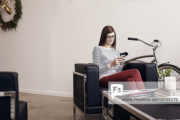 Smiling businesswoman using phone while sitting at office