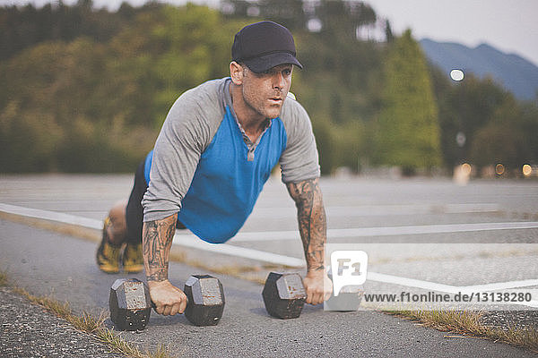 Man with dumbbells doing push-ups on road at park