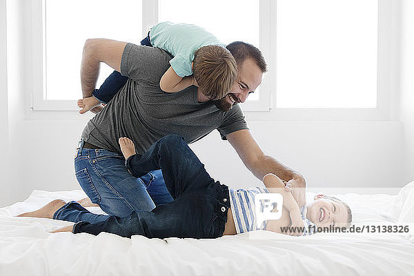 Cheerful father playing with sons on bed at home