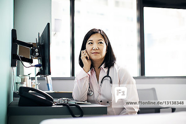Thoughtful female doctor sitting at computer desk in clinic