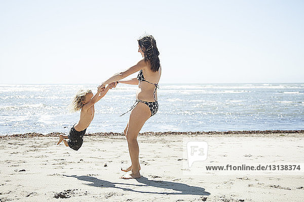 Glückliche Mutter spielt mit Tochter am Strand vor klarem Himmel