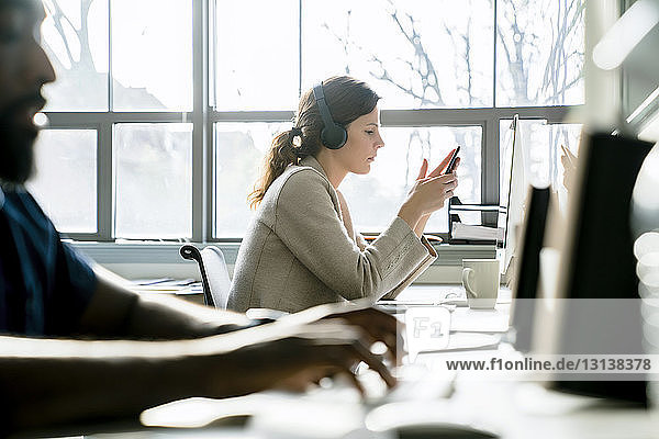 Geschäftsfrau benutzt Smartphone  während sie neben einem Kollegen im Büro sitzt