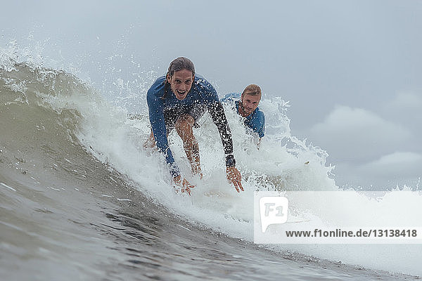Portrait of friends surfing on sea against cloudy sky