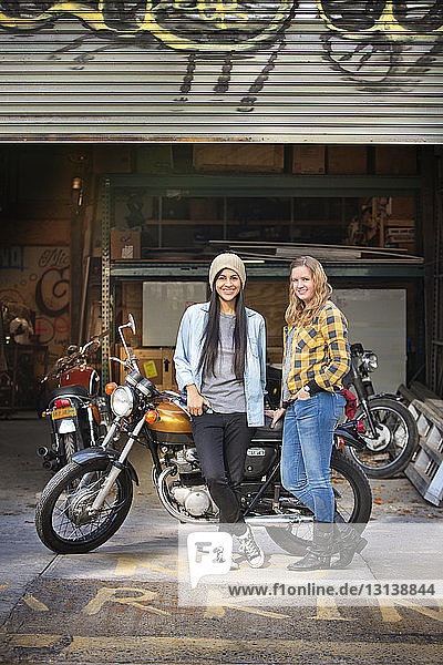 Porträt von glücklichen Besitzerinnen  die mit dem Fahrrad vor einer Autowerkstatt stehen