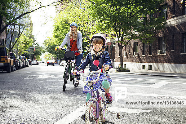 Portrait of happy mother and daughter riding bicycles on street