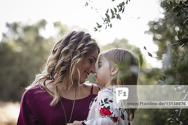 Loving mother and daughter rubbing noses by plants