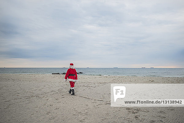 Rückansicht eines älteren Mannes im Nikolauskostüm beim Strandspaziergang