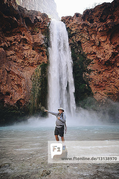 Porträt eines Mannes  der auf einem Felsen stehend gegen einen Wasserfall zeigt