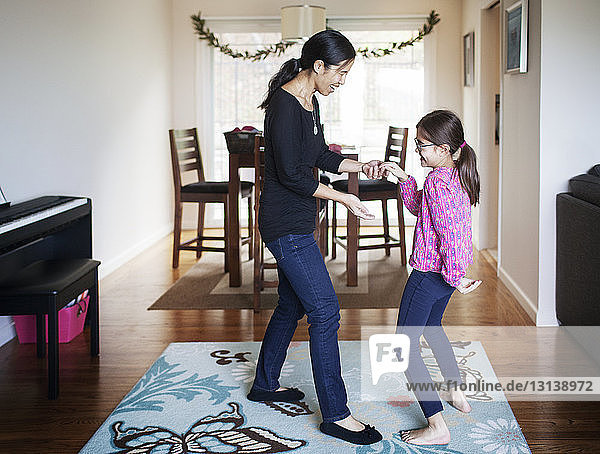 Side view of happy mother and daughter dancing at home