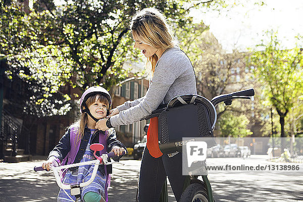 Frau hilft Tochter beim Tragen eines Fahrradhelms auf der Straße