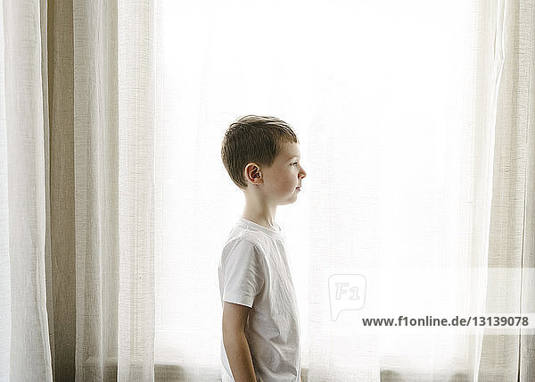 Seitenansicht eines Jungen  der zu Hause vor Vorhängen steht