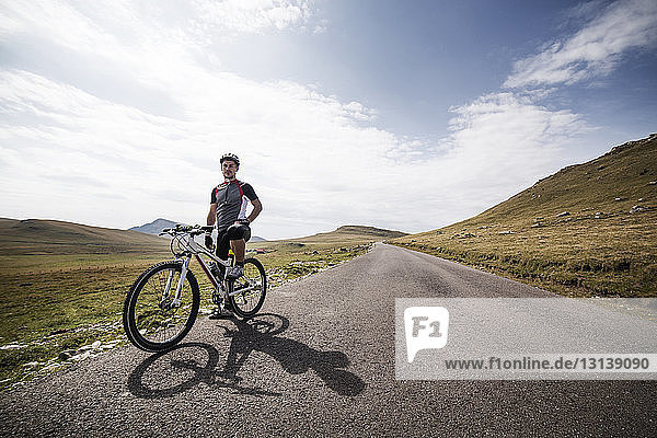 Portrait of man standing with bicycle on road against cloudy sky
