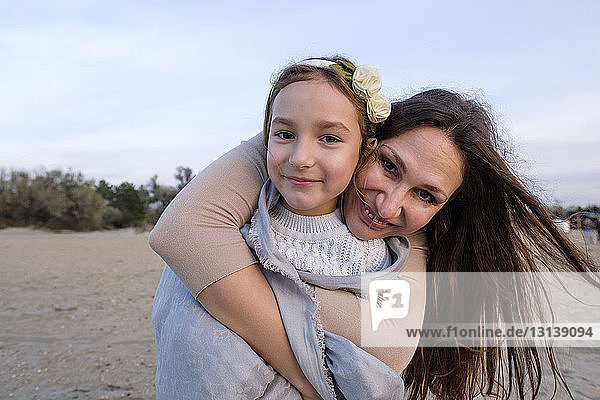 Portrait of smiling mother embracing daughter while standing at beach against sky