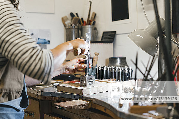 Mittelteil eines Handwerkers  der mit Handwerkzeugen arbeitet  während er in einer Werkstatt Schmuck auf dem Tisch herstellt
