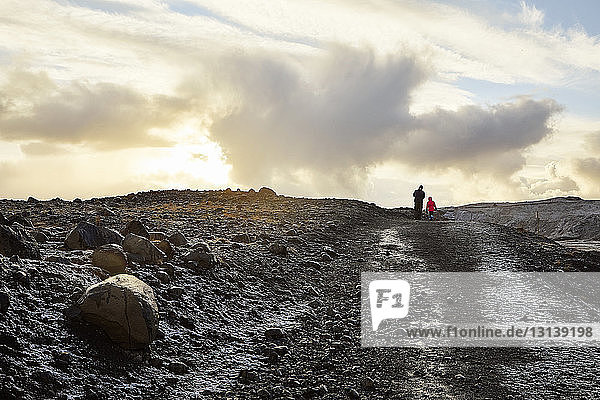 Rear view of father with daughter walking on mountain against cloudy sky