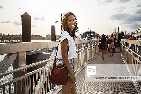Portrait of smiling woman walking on pier against sky