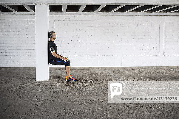 Side view of male athlete doing wall sit exercise in parking lot