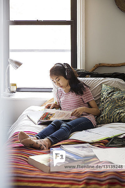 Teenage girl studying with headphones on bed at home