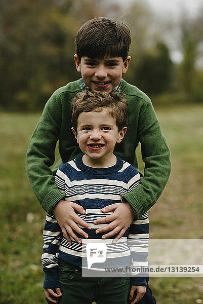 Portrait of smiling brothers standing on grassy field at park