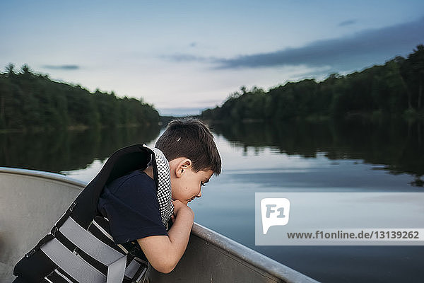 Side view of boy wearing life jacket while sitting in boat on lake