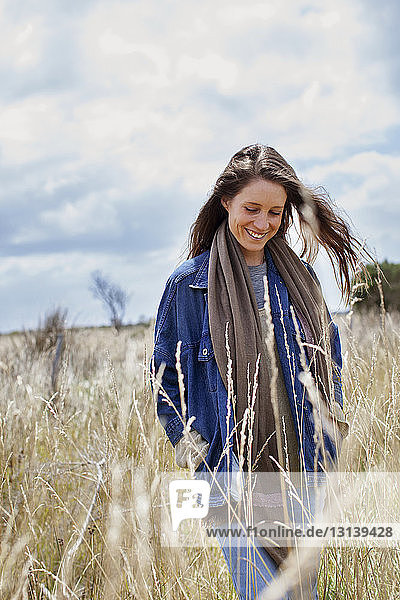 Woman smiling while walking on field against sky