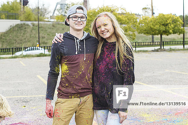 Portrait of happy friends with powder paint standing on footpath at park