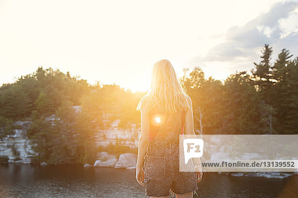 Rückansicht einer Frau  die bei Sonnenuntergang am See steht