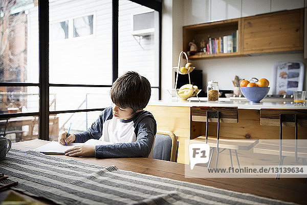 Junge schreibt in Buch auf Tisch zu Hause