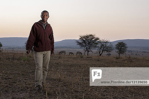 Porträt eines lächelnden Mannes  der auf einem Grasfeld im Serengeti-Nationalpark gegen den Himmel steht