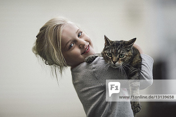 Portrait of cute girl holding tabby cat at home