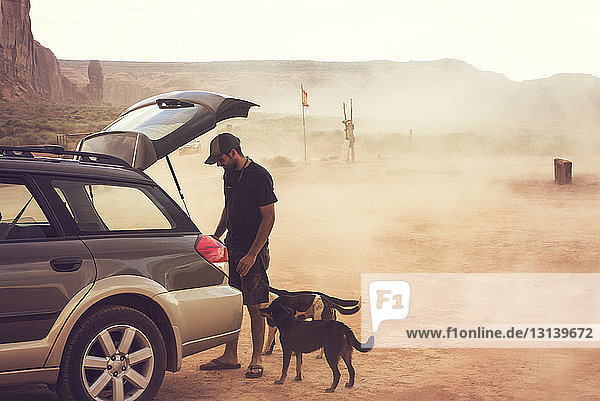 Mann steht mit Hunden und schaut in den Kofferraum eines Autos auf dem Feld