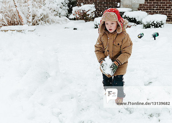 Cute boy looking down while making snowball in yard