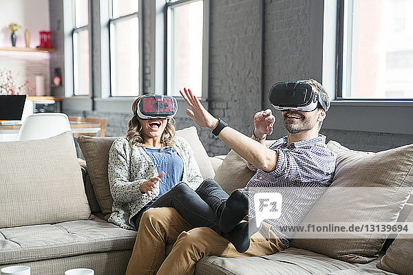 Colleagues wearing virtual reality simulator while sitting on sofa in office