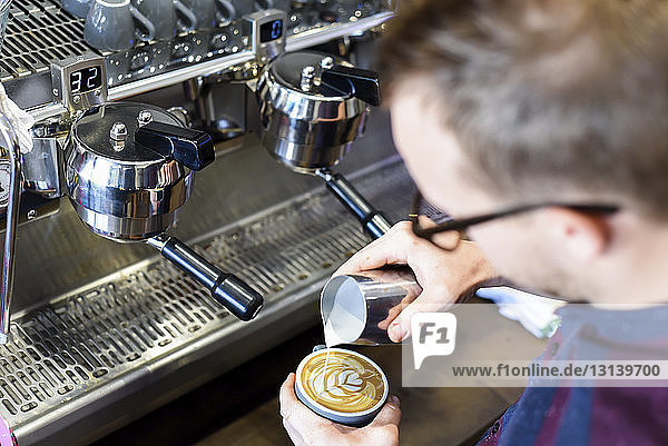 Barista gießt Milch in Kaffee  während er im Café ein schaumiges Getränk zubereitet