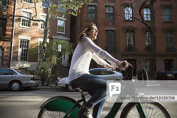 Side view of cheerful woman riding bicycle on street