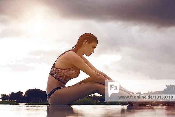 Side view of beautiful woman sitting on floor against cloudy sky