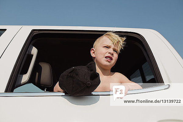 Low angle view of boy looking through window while sitting in vehicle against clear sky