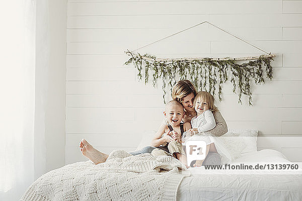 Glückliche Mutter mit Kindern zu Hause im Bett sitzend